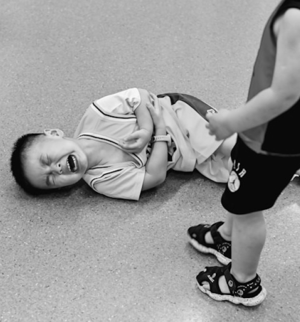 Crying child lying on the floor holding their stomach.
