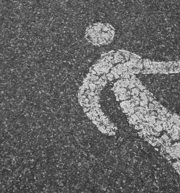 Worn pedestrian symbol painted on asphalt.
