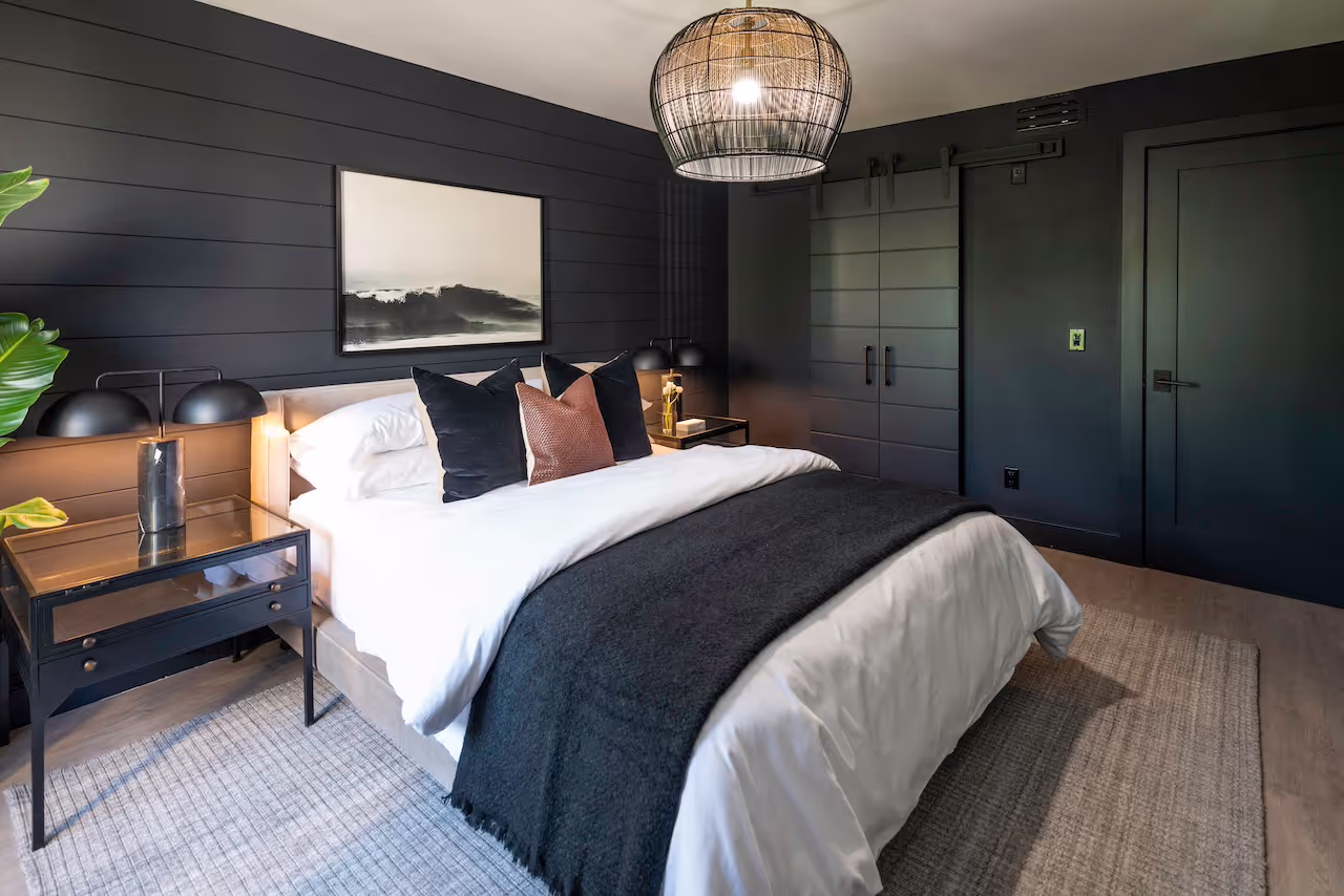 Modern bedroom with dramatic black feature wall, pendant lighting, and custom built-ins showcased in Howie Mandel’s Celebrity IOU remodel. Cabinetry by Marvel Cabinetry for HGTV’s Property Brothers: Celebrity IOU - Howie Mandel