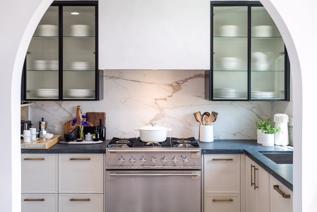 Light and airy kitchen with arched upper cabinets, marble backsplash, glass door cabinetry, and custom storage featured in Gwyneth Paltrow’s Celebrity IOU renovation. Cabinetry by Marvel Cabinetry for HGTV’s Property Brothers: Celebrity IOU - Gwyneth Paltr