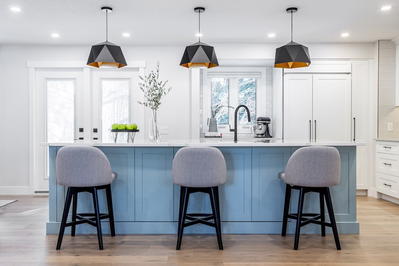 Kitchen with soft blue island cabinetry, white perimeter cabinets, pendant lighting, and elegant millwork detailing. Cabinetry by Marvel Cabinetry.