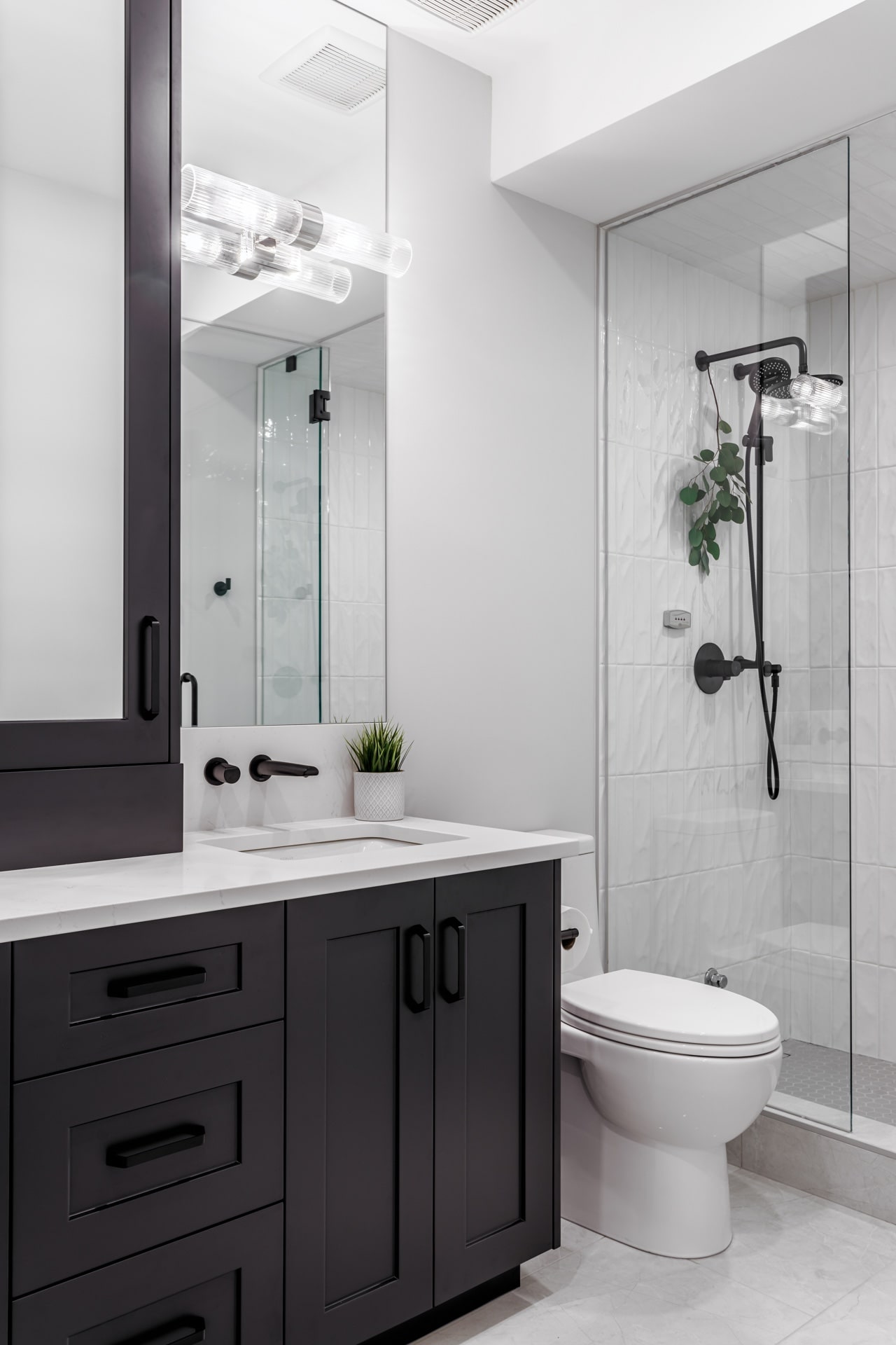 Bathroom with dark double vanity cabinetry, quartz counters, glass shower, and elegant hardware. Cabinetry by Marvel Cabinetry.