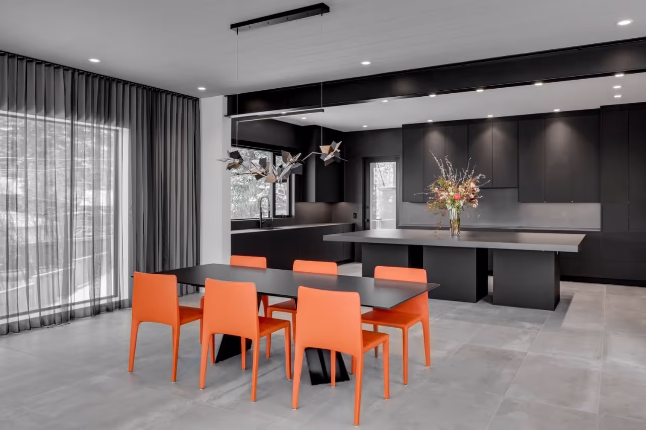 Open-concept dining area with custom black cabinetry, large windows, and bold orange seating. Cabinetry by Marvel Cabinetery.