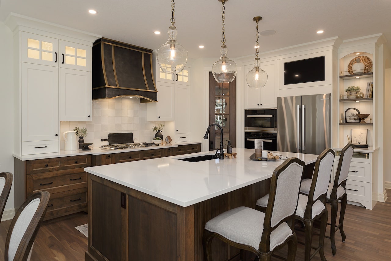 Traditional kitchen with custom dark island cabinetry, brass hardware, decorative hood, and white perimeter cabinets. Cabinetry by Marvel Cabinetry.