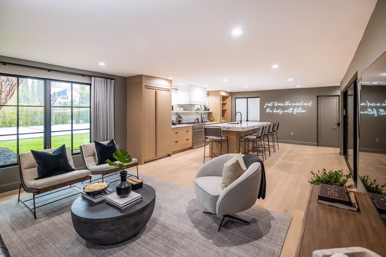 Contemporary living space connected to a custom kitchen with wood cabinetry and open shelving in Kevin Hart’s Celebrity IOU project. Cabinetry by Marvel Cabinetry for HGTV’s Property Brothers: Celebrity IOU - Kevin Hart