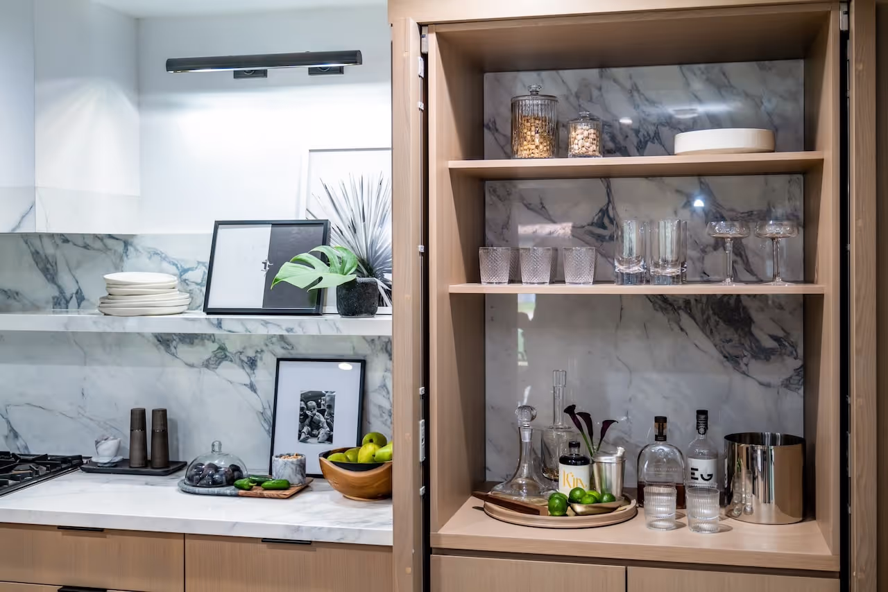 Luxury glass-front bar cabinet with integrated storage, lighting, and marble backsplash featured in Kevin Hart’s Celebrity IOU renovation. Cabinetry by Marvel Cabinetry for HGTV’s Property Brothers: Celebrity IOU - Kevin Hart
