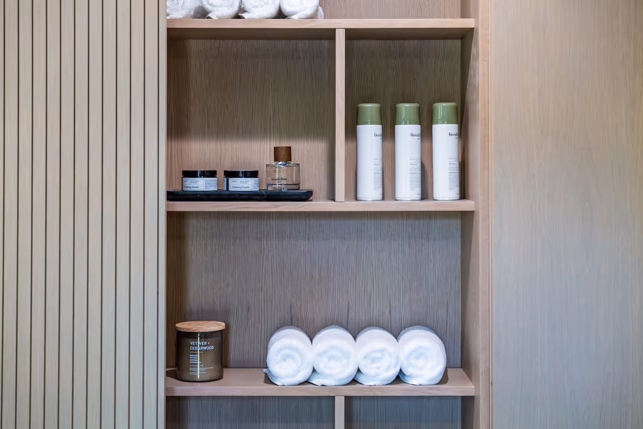 Custom shelving with grooming products and warm wood finishes, part of the barbershop build created for Kevin Hart’s Celebrity IOU project. Cabinetry by Marvel Cabinetry for HGTV’s Property Brothers: Celebrity IOU - Kevin Hart