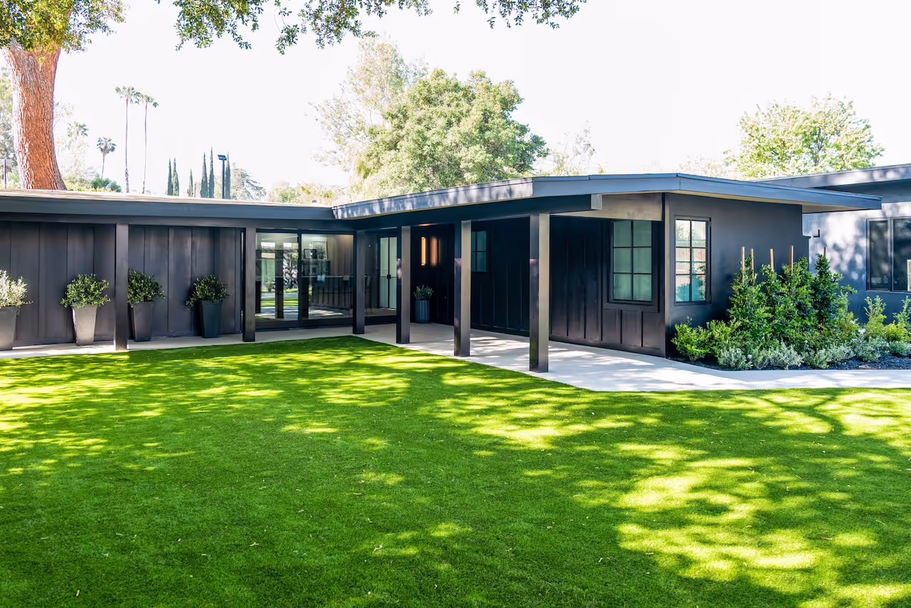Exterior view of the completed modern studio with dark siding, custom windows, and landscaped yard from Kevin Hart’s Celebrity IOU reveal. Cabinetry by Marvel Cabinetry for HGTV’s Property Brothers: Celebrity IOU - Kevin Hart