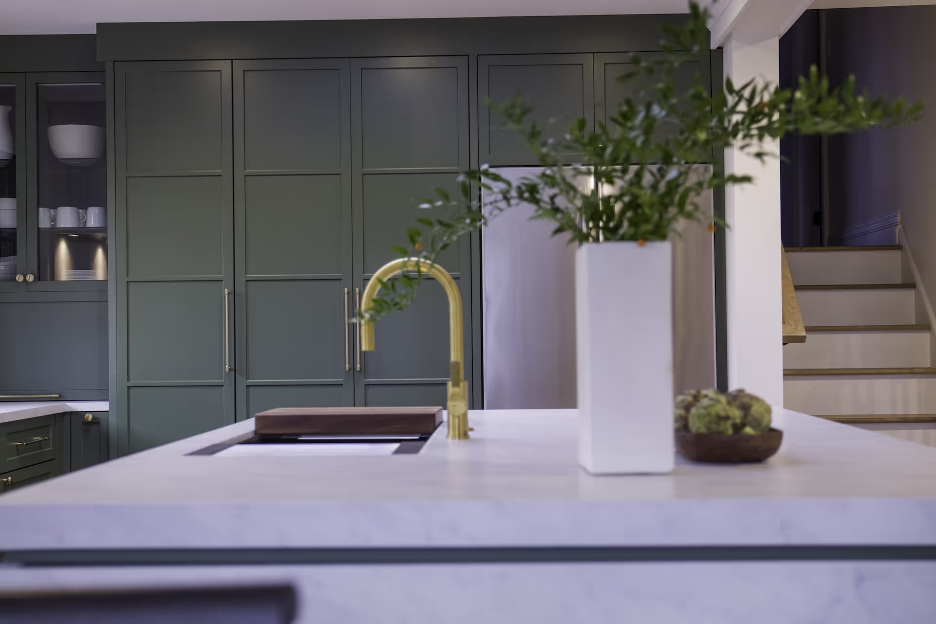 Luxury kitchen featuring deep green custom cabinetry, marble island, gold faucet, and modern open-concept design from Melissa McCarthy’s Celebrity IOU makeover. Cabinetry by Marvel Cabinetry for HGTV’s Property Brothers: Celebrity IOU - Melissa McCarthy