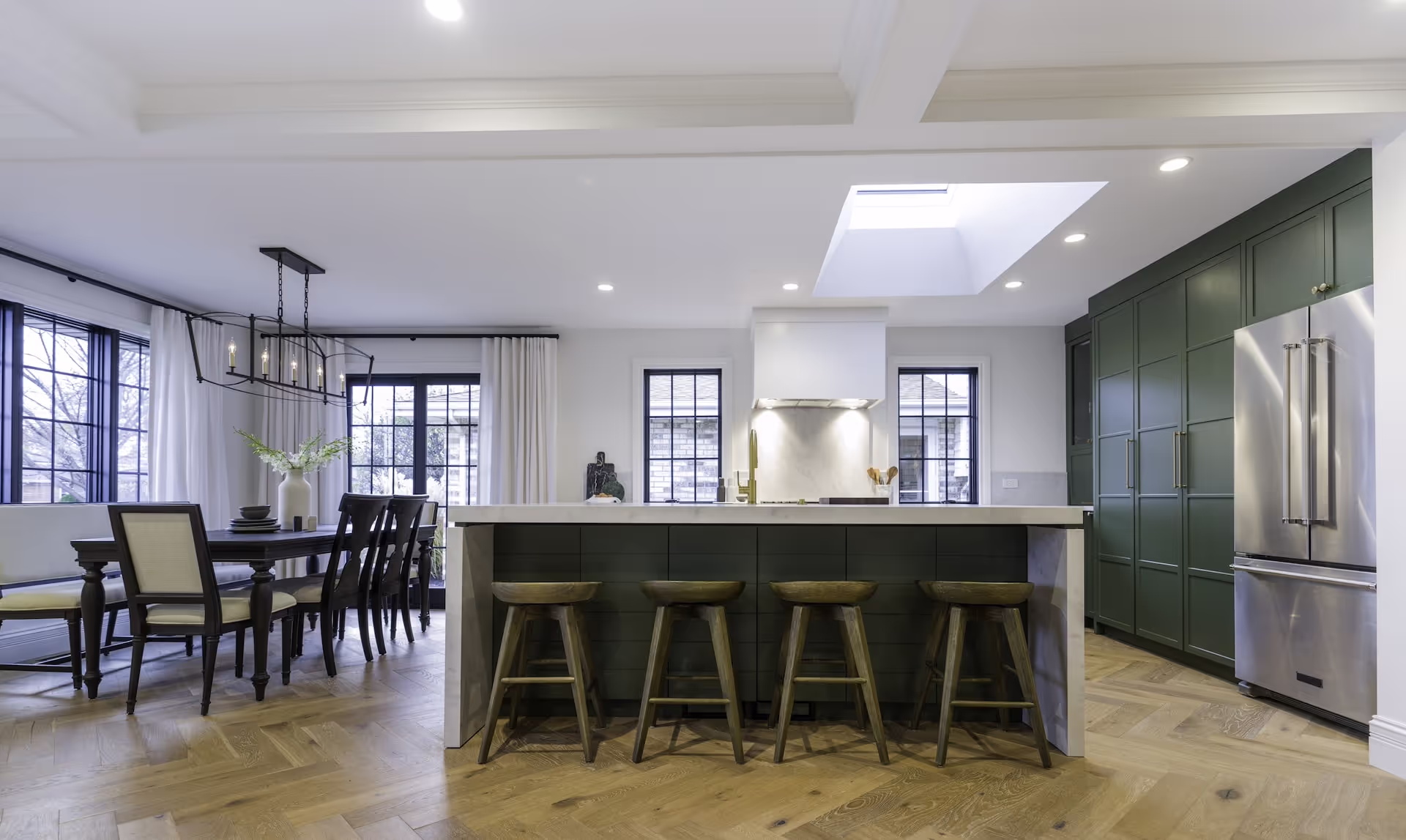 Open kitchen and dining area showcasing large island, custom green cabinetry, and modern ceiling details from Melissa McCarthy’s Celebrity IOU project. Cabinetry by Marvel Cabinetry for HGTV’s Property Brothers: Celebrity IOU - Melissa McCarthy