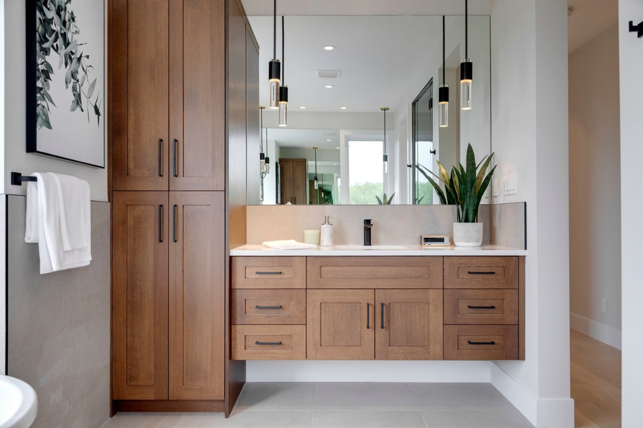 Warm wood double vanity with integrated storage, large mirrors, and modern bathroom design. Cabinetry by Marvel Cabinetry.