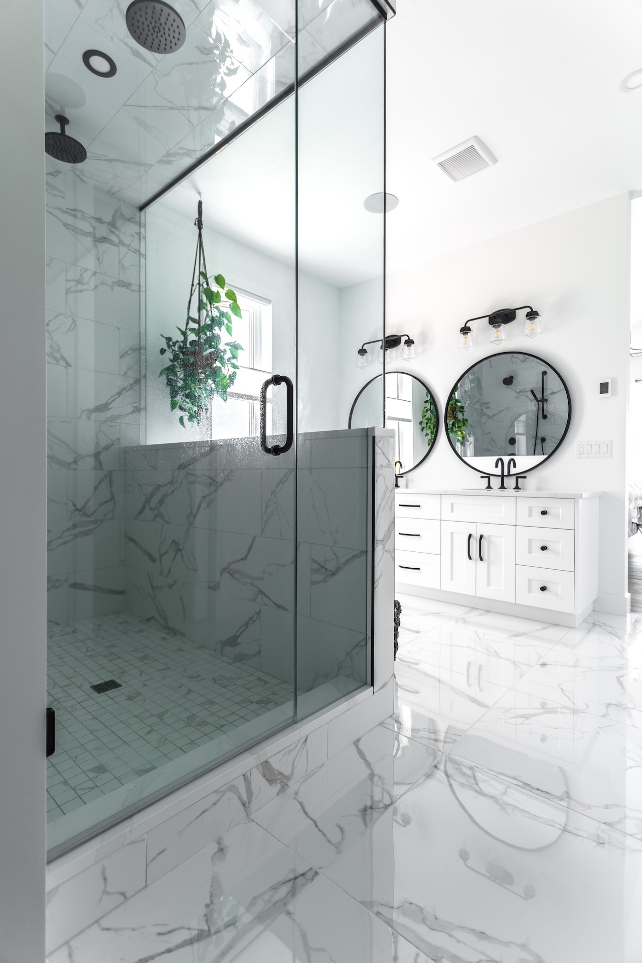 Spa-inspired bathroom featuring custom white vanity cabinetry, glass shower enclosure, and marble-look surfaces. Cabinetry by Marvel Cabinetry.