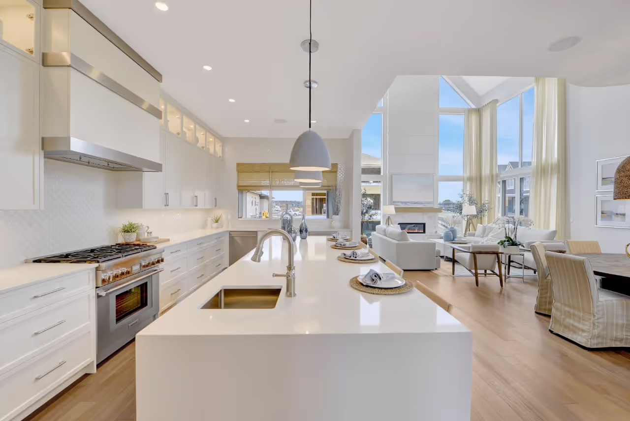 Bright luxury kitchen with large island, white custom cabinetry, pendant lighting, and high-end appliances. Cabinetry by Marvel Cabinetry.