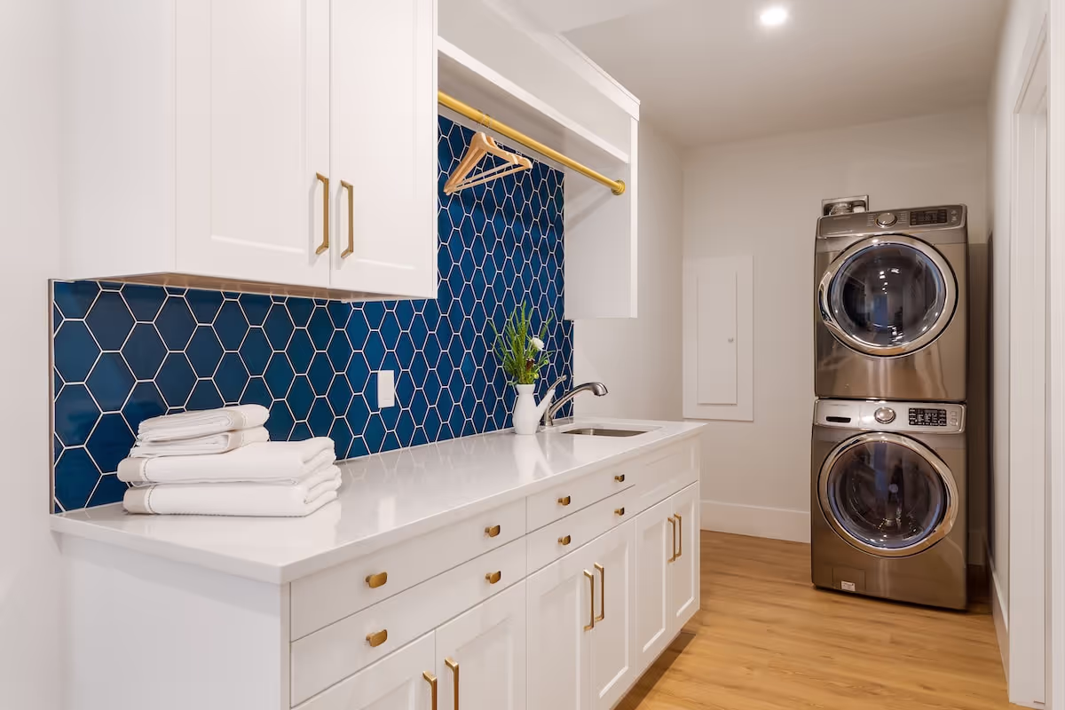 Laundry room with custom white cabinetry, blue tile backsplash, and stacked washer-dryer integration. Cabinetry by Marvel Cabinetry.