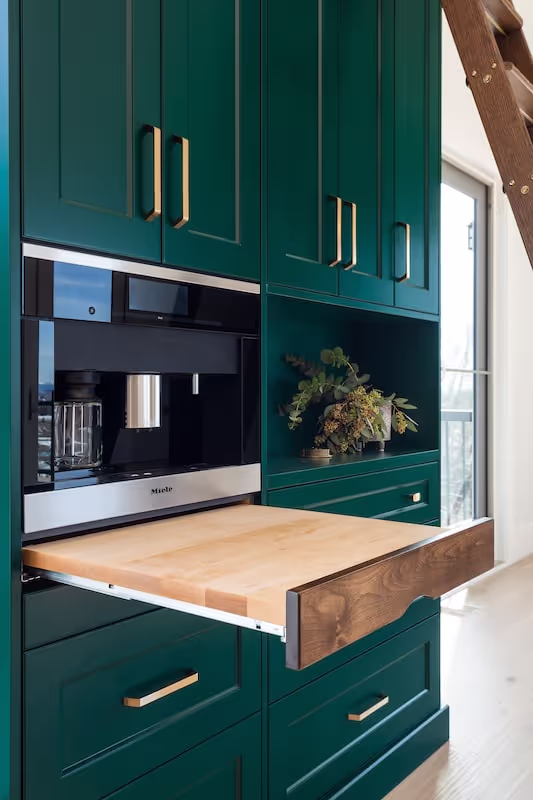 Close-up of custom green kitchen cabinetry with appliance integration, pull-out cutting board, and premium storage solutions. Cabinetry by Marvel Cabinetry.