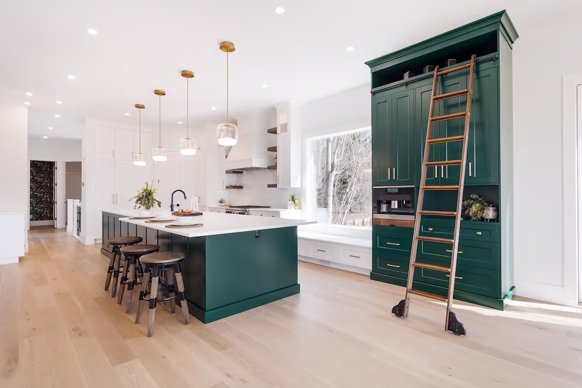 Bright kitchen with full-height white cabinetry, custom green island with seating, and designer lighting. Cabinetry by Marvel Cabinetry.