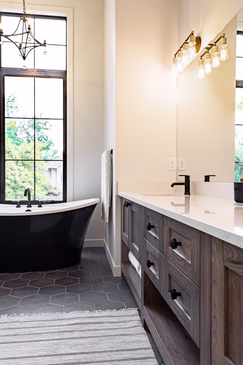 Modern bathroom with dark freestanding tub, custom wood vanity cabinetry, and refined lighting in a spa-inspired design. Cabinetry by Marvel Cabinetry.