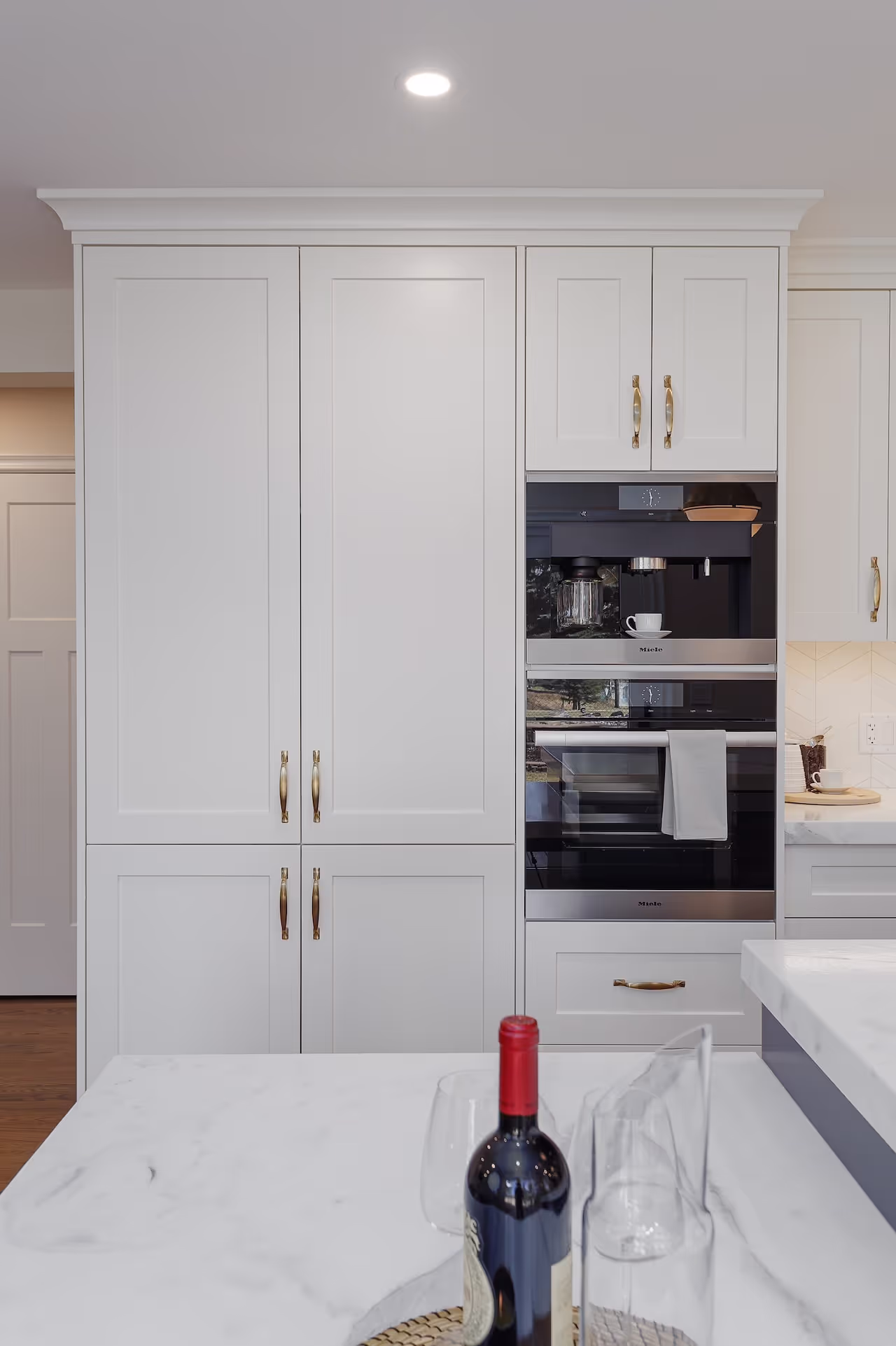 Tall white pantry cabinets with integrated appliances and elegant millwork detailing. Cabinetry by Marvel Cabinetry.