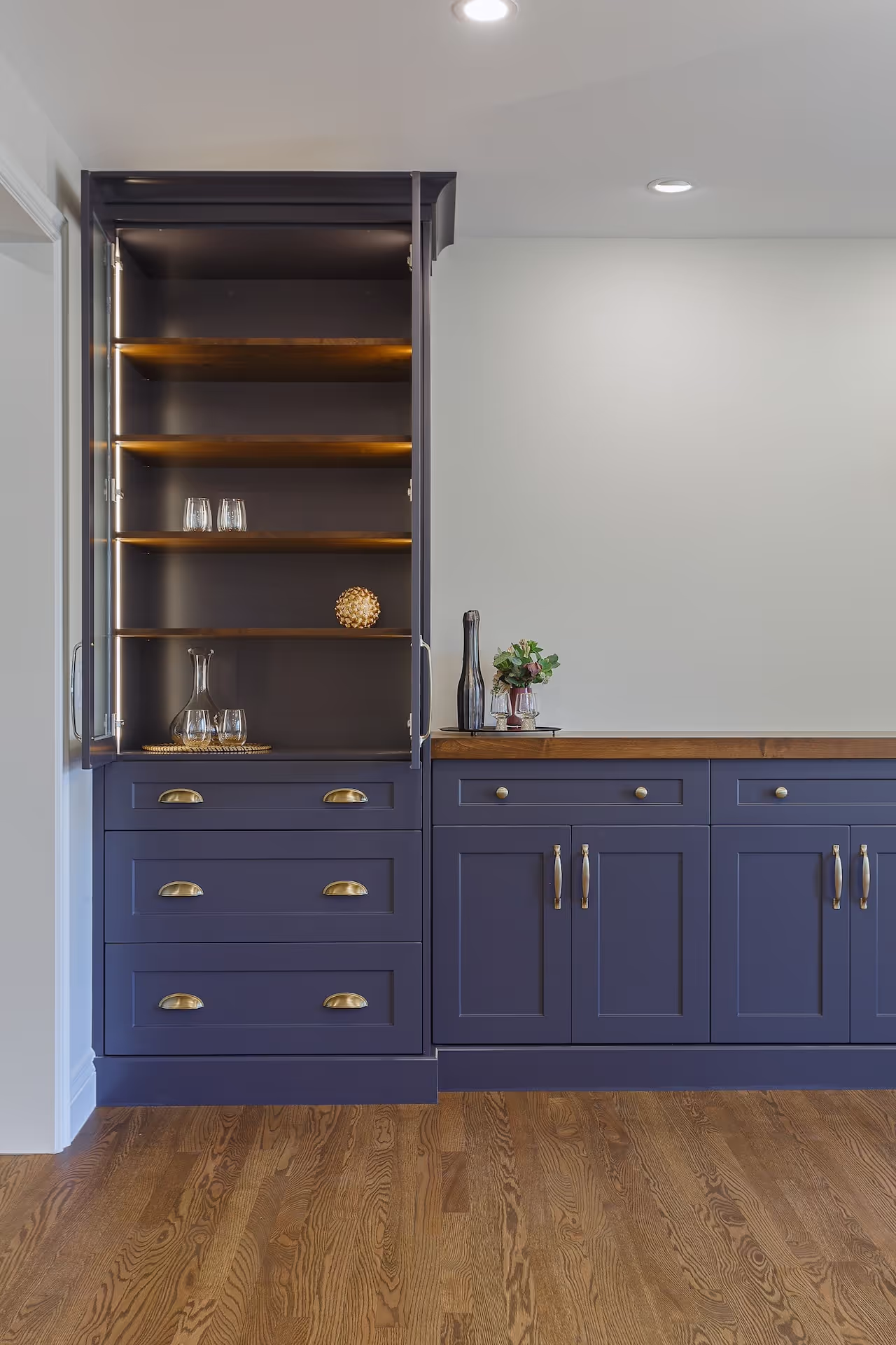 Custom navy built-in bar with open shelving, brass hardware, and wood floors for a high-end home interior. Cabinetry by Marvel Cabinetry.