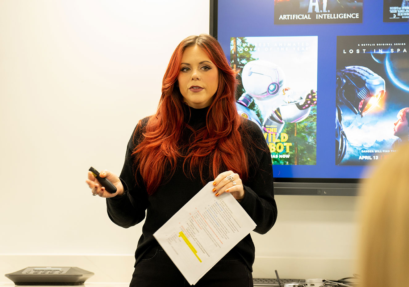 Woman with red hair standing in front of a screen while delivering a presentation