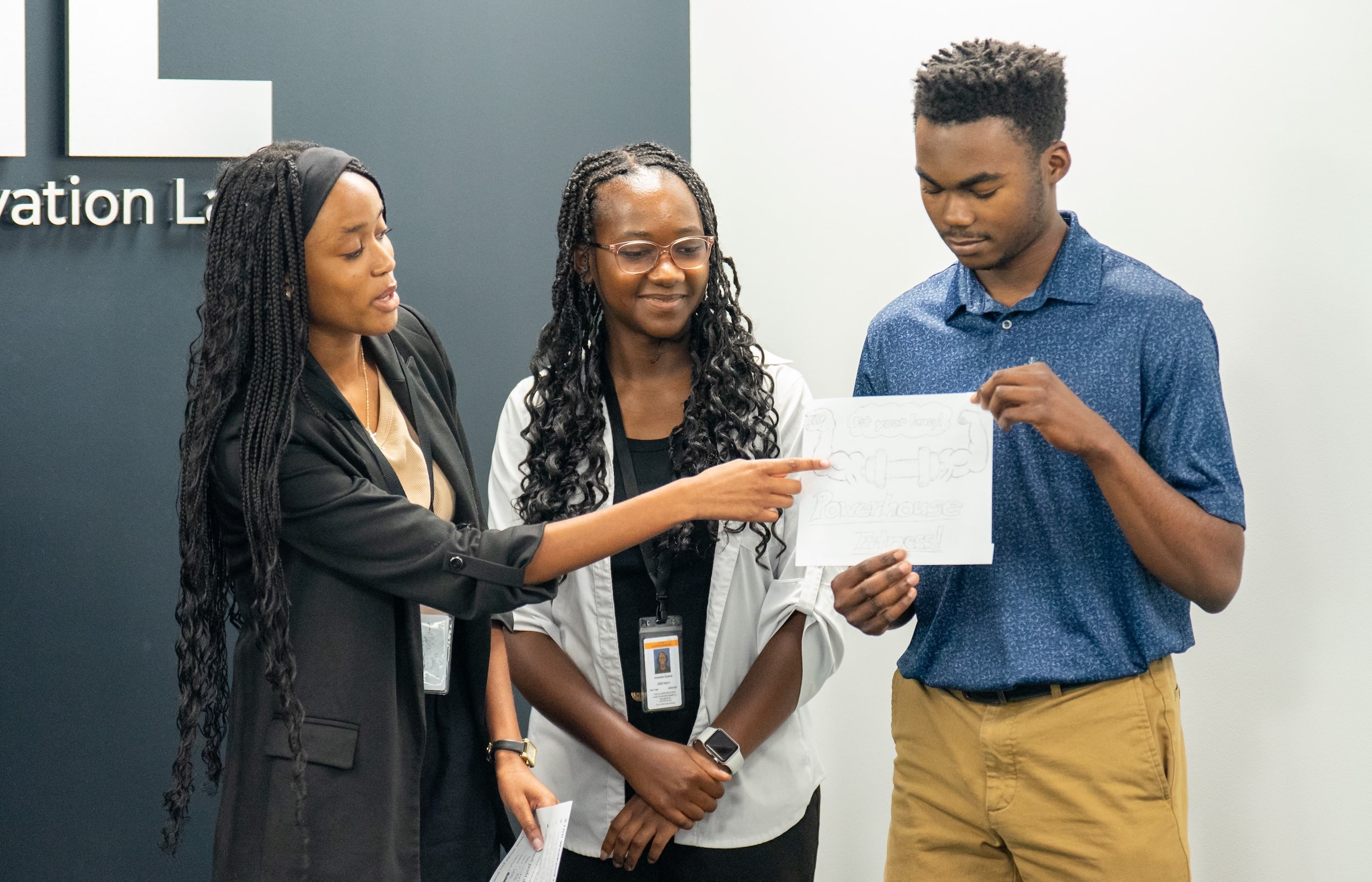 Students of color smiling and pointing at a piece of paper together
