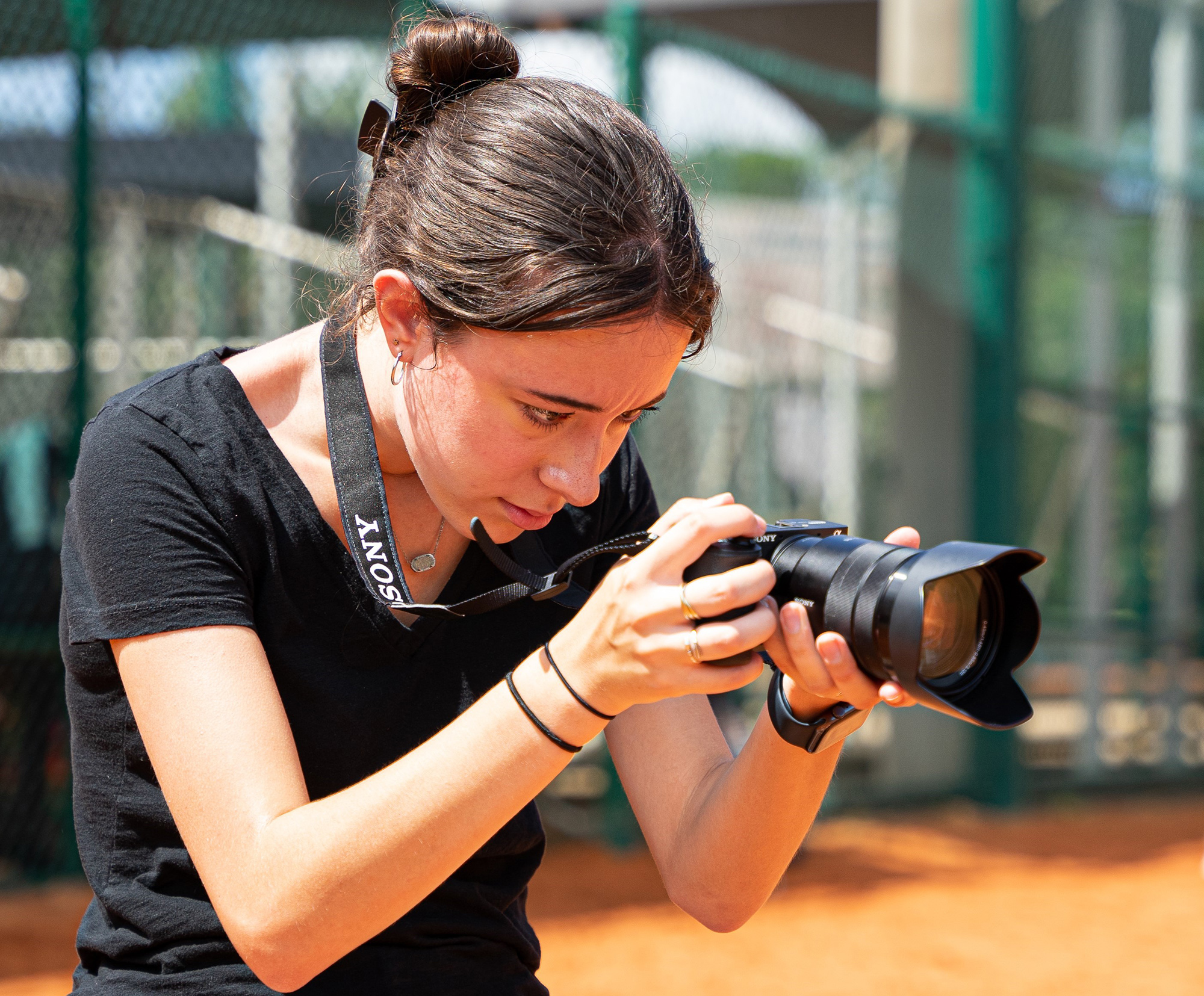 Summer student intern holding a camera and taking photos on a softball field