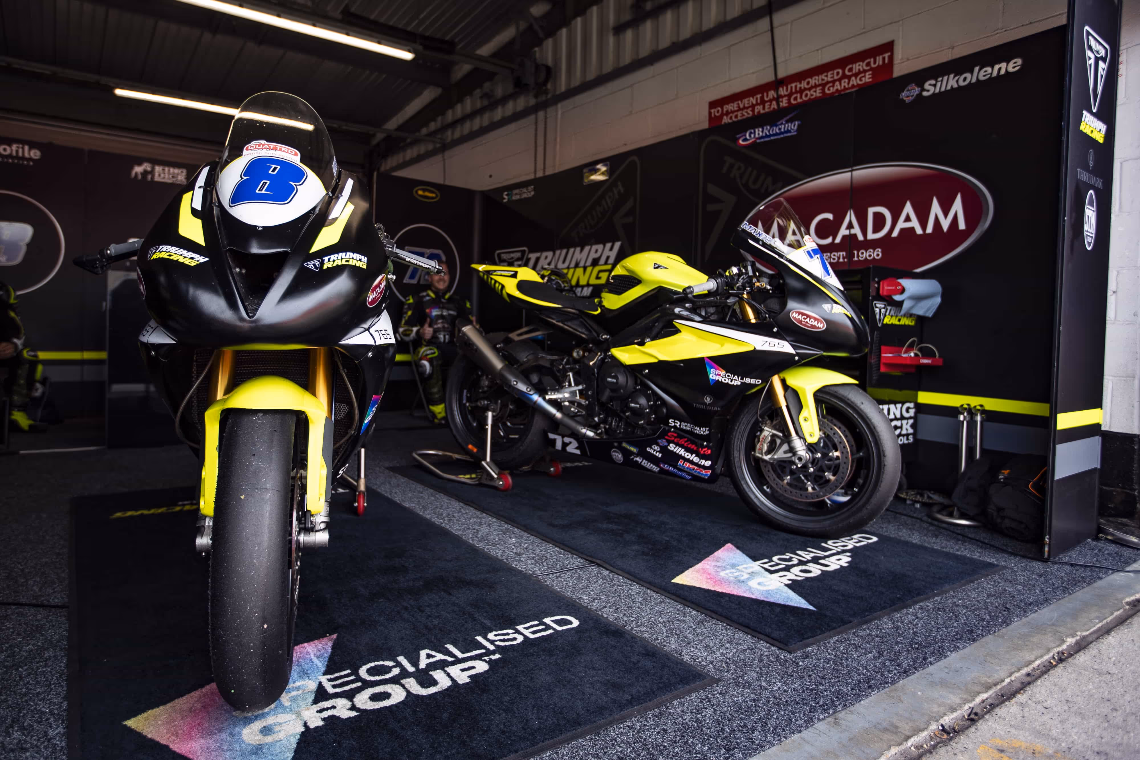 Two racing motorcycles in yellow and black in a garage pit