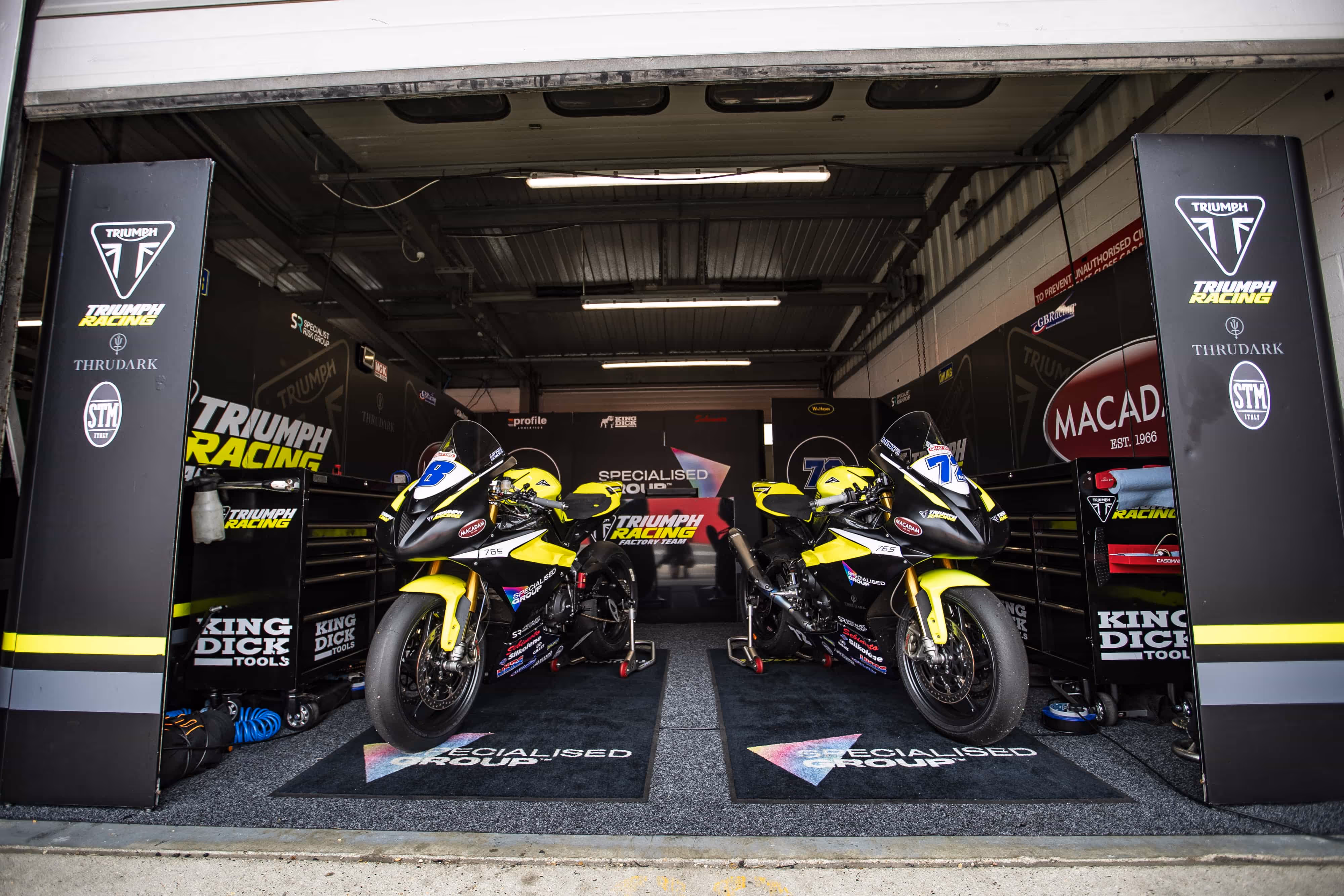 Two Triumph racing motorcycles in a professional motorsport garage setup