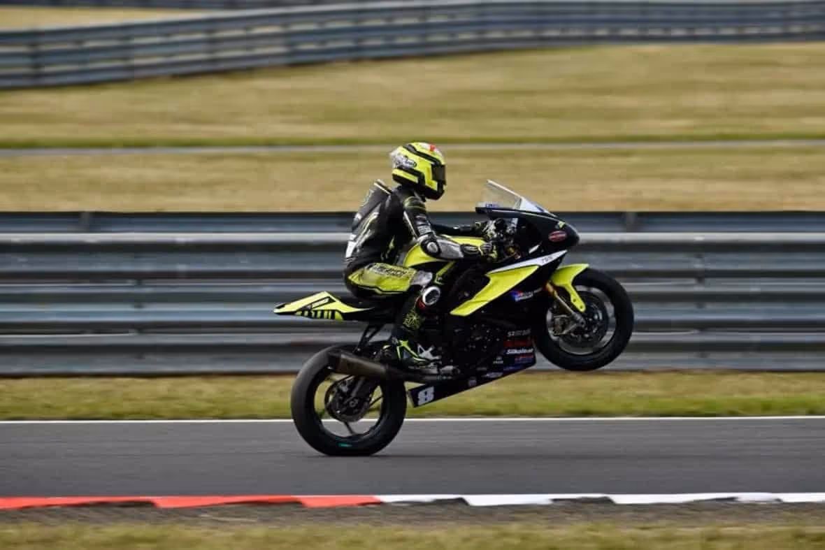 Motorcycle racer performing wheelie on yellow and black sports bike