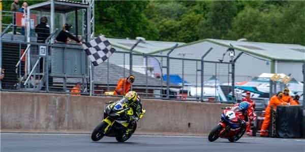 Motorcycle racers near finish line with checkered flag and track officials