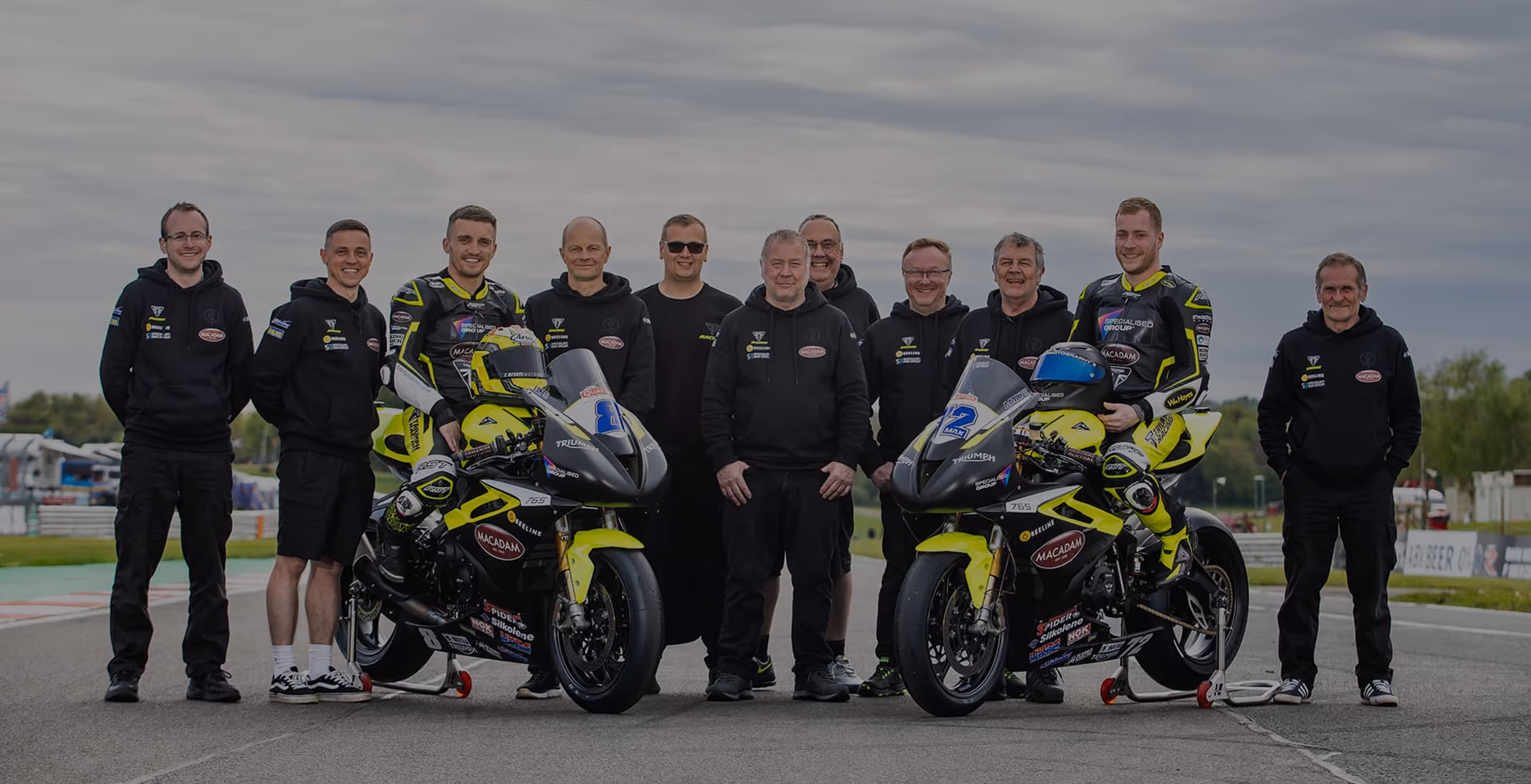 Racing team with motorcycles posing on track in black and yellow uniforms