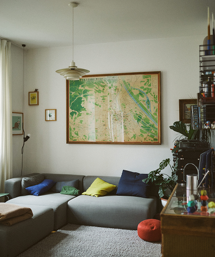Stilvoll eingerichtetes, helles Wohnzimmer, mit grauer Couch und großem Bild an der Wand.