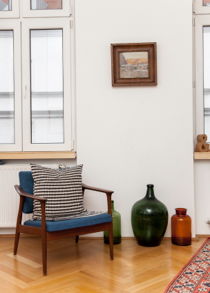 Ansicht eines hellen Zimmers mit Parkettboden und einem dunklen Holzstuhl und bunten Glasvasen.