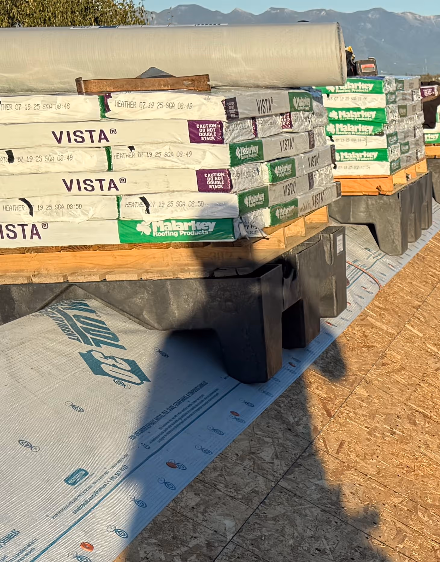 Stacked pallets of Malarkey Vista roofing shingles on a rooftop with mountains in the background.