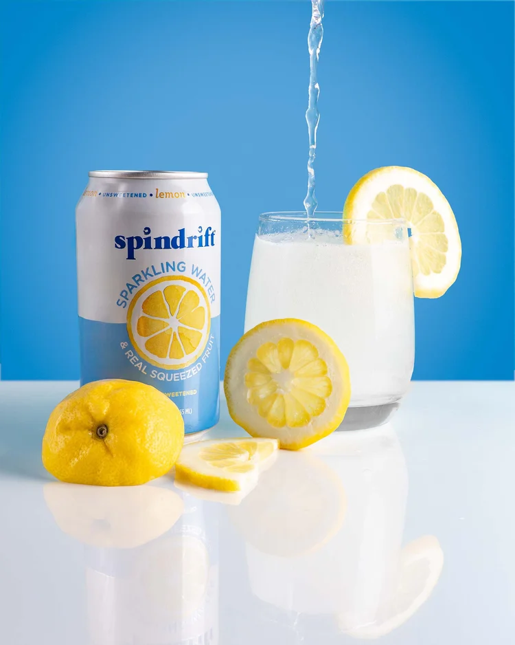 Pouring Spindrift Lemon Sparkling Water into a glass with fresh lemons.