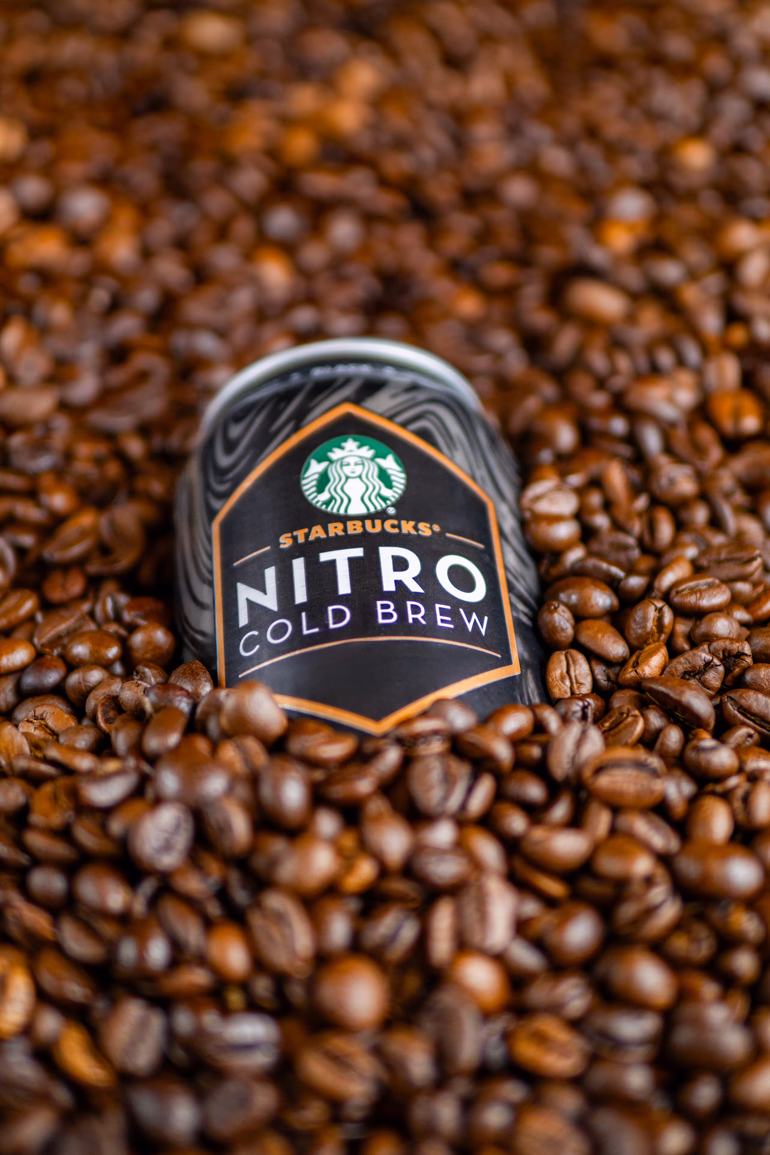 A can of Starbucks Nitro Cold Brew nested in a pile of roasted coffee beans.