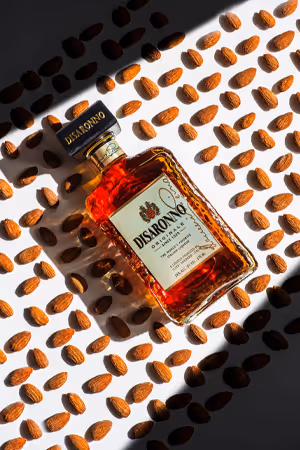 Disaronno bottle on coffee-bean pattern with striped shadows, product photography by Photos by Lars.