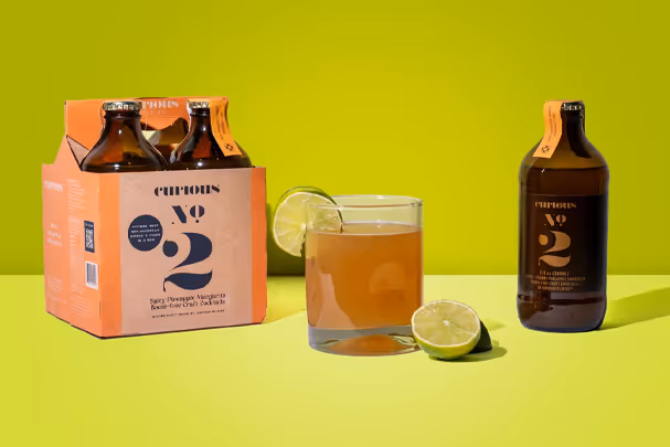 Curious No.2 cocktail kit with bottle, glass, and lime slices on lime-green set, beverage photography by Photos by Lars.