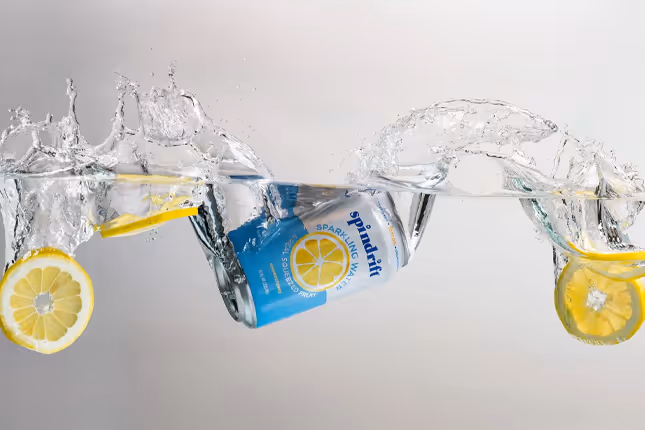Spindrift Lemon sparkling water can splashing through water with lemon slices, beverage photography by Photos by Lars.