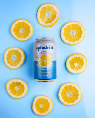 Spindrift Lemon sparkling water can surrounded by lemon slices on blue backdrop, beverage photography by Photos by Lars.