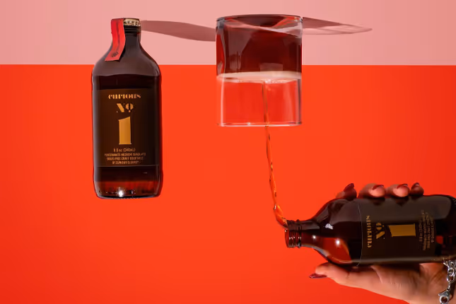 Curious bottle pouring into a suspended glass on red backdrop, beverage photography by Photos by Lars.
