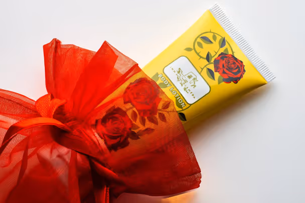 Floral body lotion tube wrapped in red tulle on white surface, product photography by Photos by Lars.