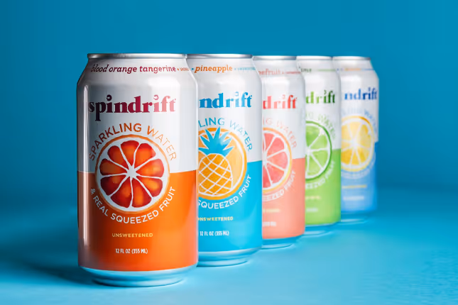 Spindrift sparkling water cans lined up on blue background, beverage photography by Photos by Lars.
