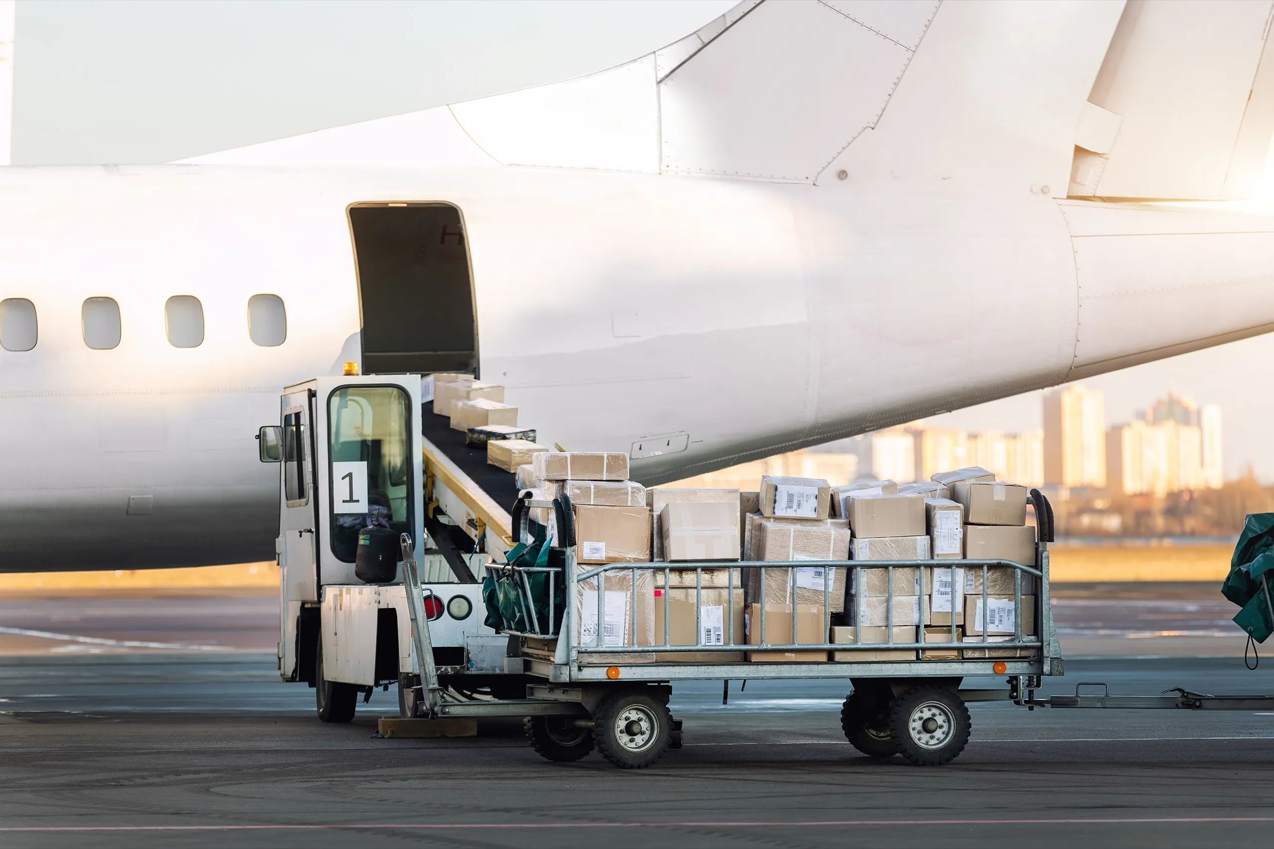 Cargo cart loaded with boxes next to an airplane being loaded via a conveyor belt.