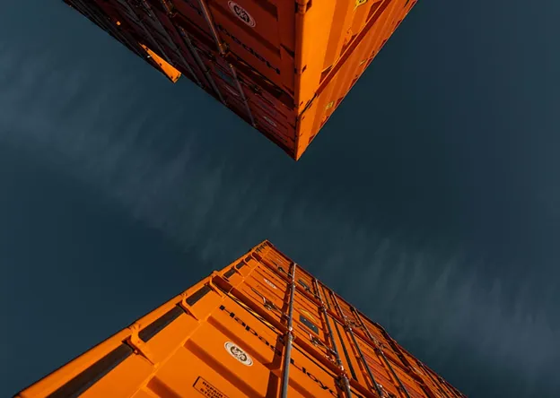View looking up at two stacked orange shipping containers under a dark sky.
