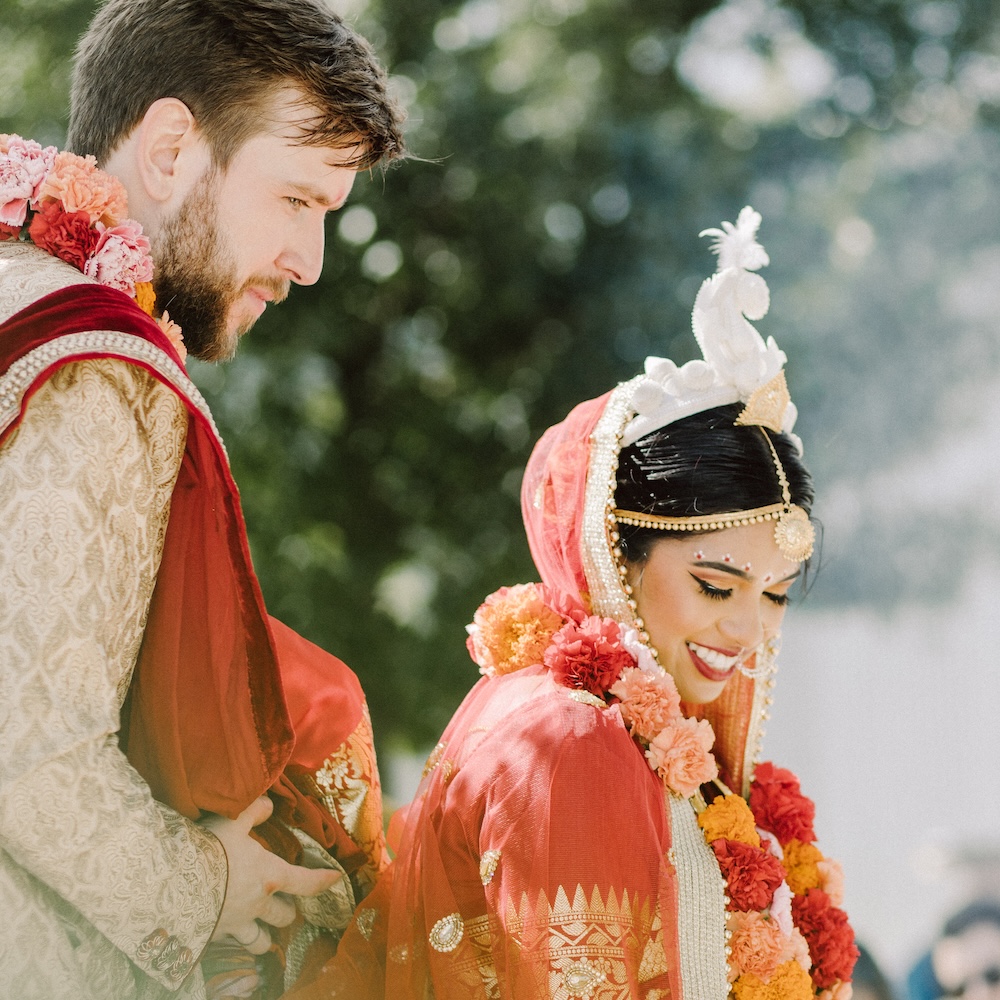 Bride and groom dressed in traditional attire exchanging joyful smiles during a wedding ceremony.