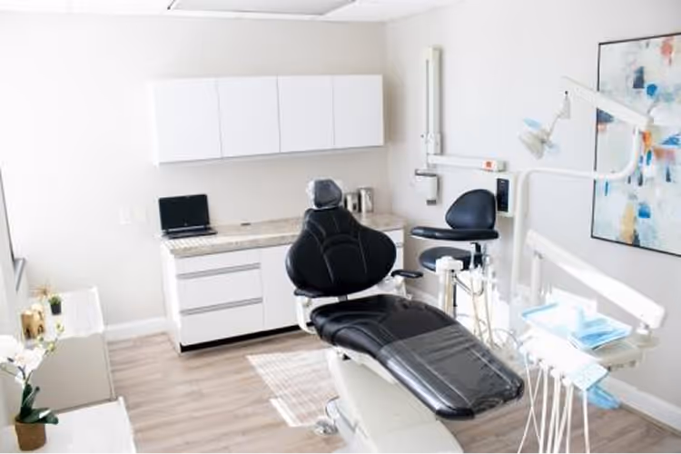 Clean, modern dental office with black dental chair, white cabinets, and dental equipment.