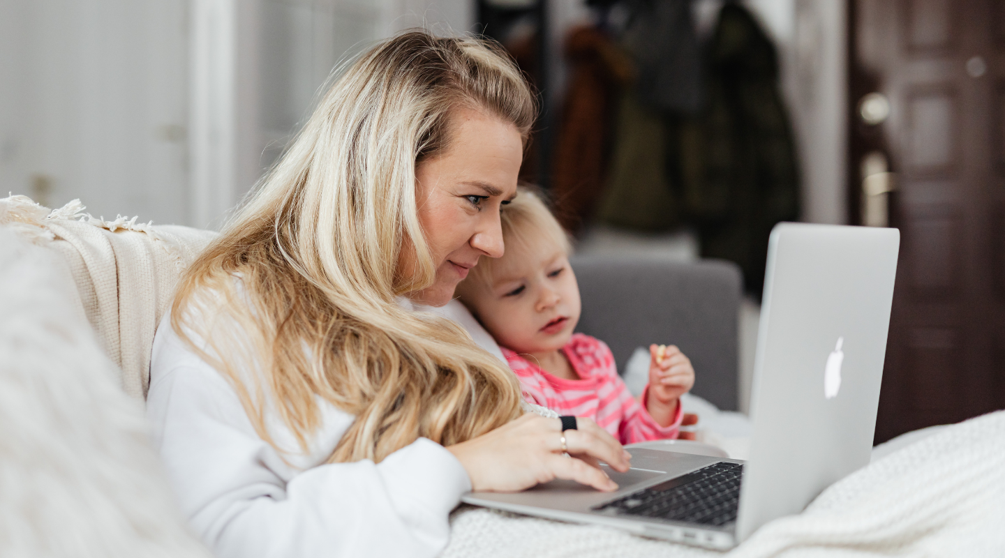 Parent working on a laptop at home while holding a child, planning household finances and future savings.