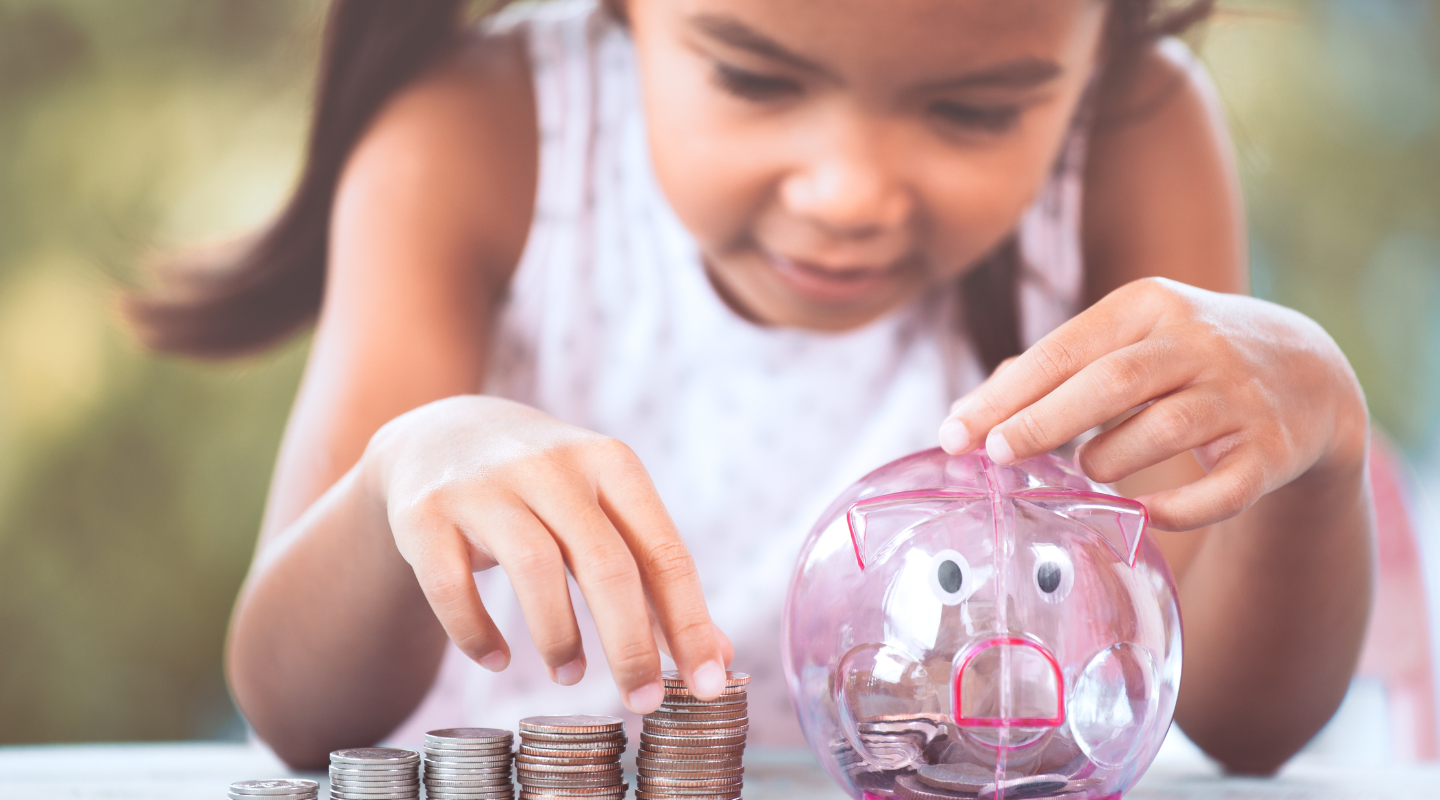 Child placing coins into a piggy bank, representing savings and long term financial planning for kids.