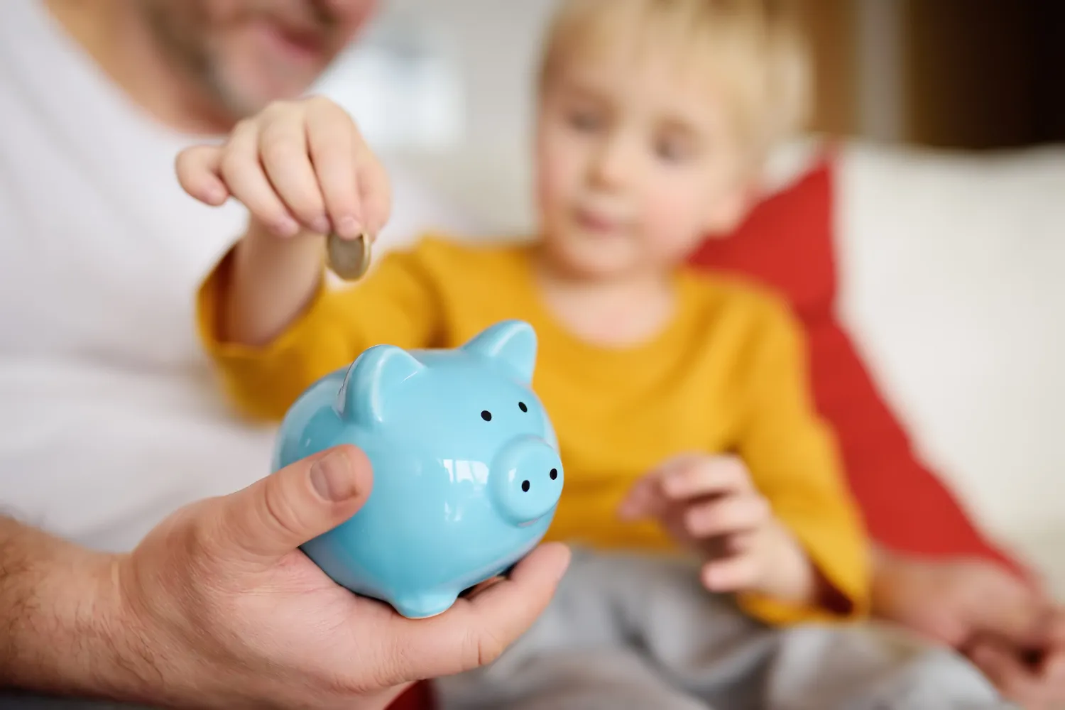 Parent and child putting a coin into a blue piggy bank